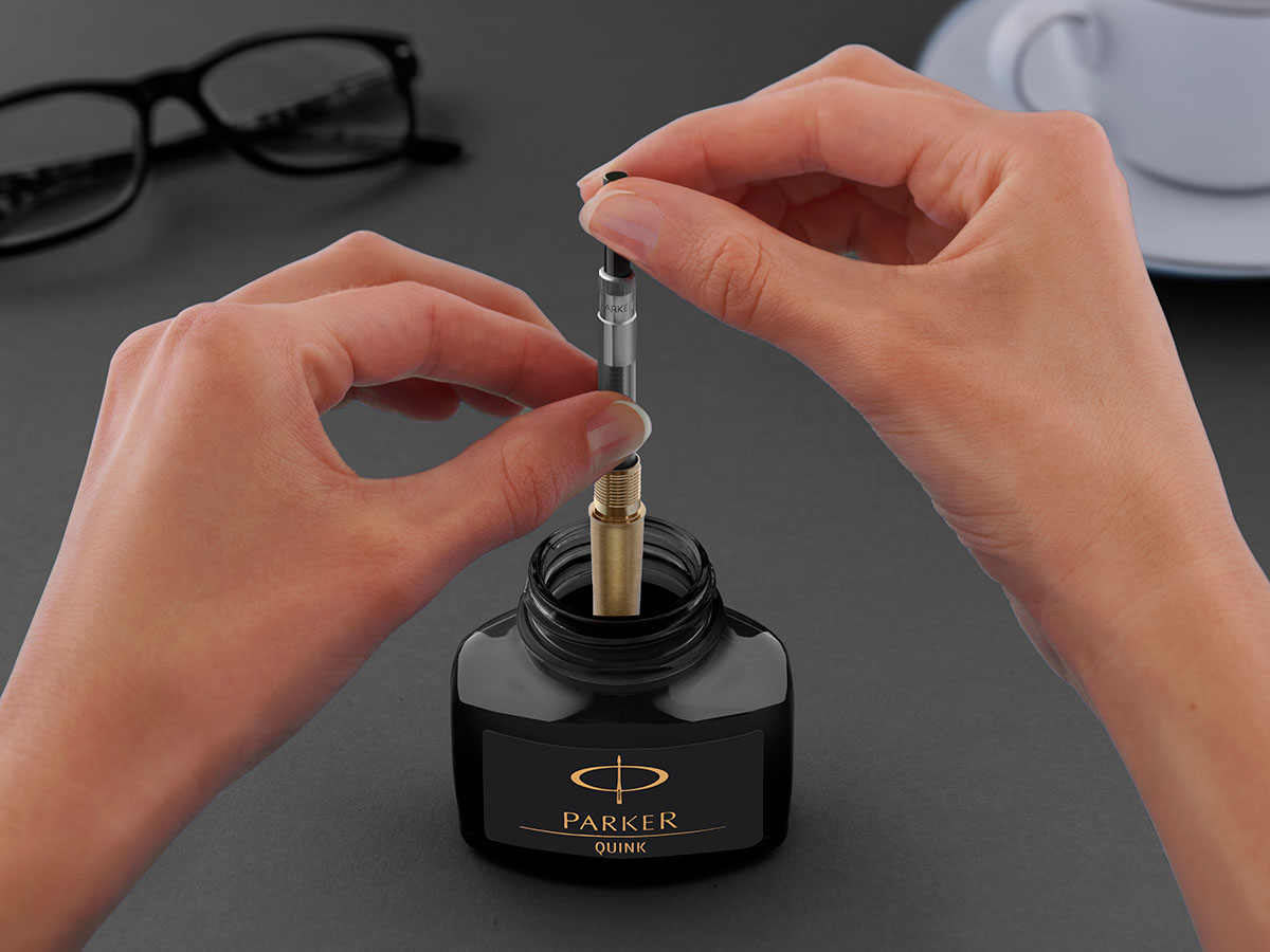 Ręce napełniające pióro wieczne Parker atramentem z butelki Parker Quink za pomocą tłoczka.