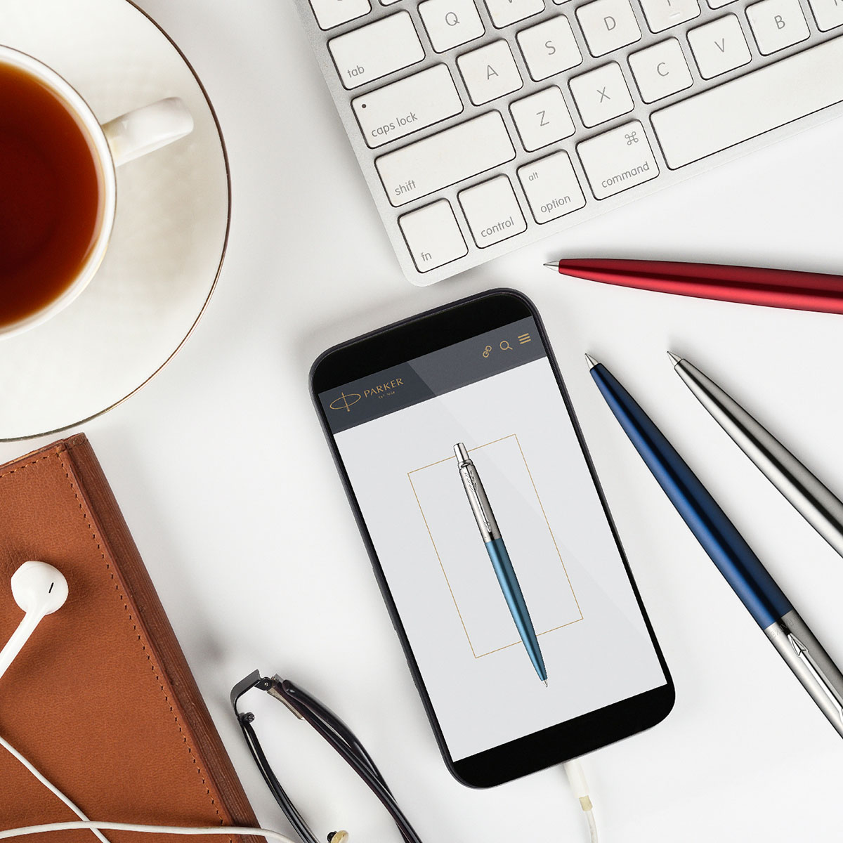 Długopis Parker Jotter Waterloo Blue CT obok smartfona z katalogiem Parker, filiżanki z herbatą i klawiatury, aranżacja biurkowa