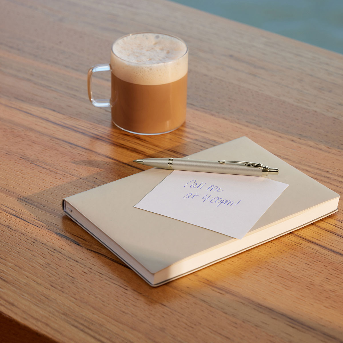 Długopis Parker IM Monochrome Champagne położony na notesie obok filiżanki kawy na drewnianym stole