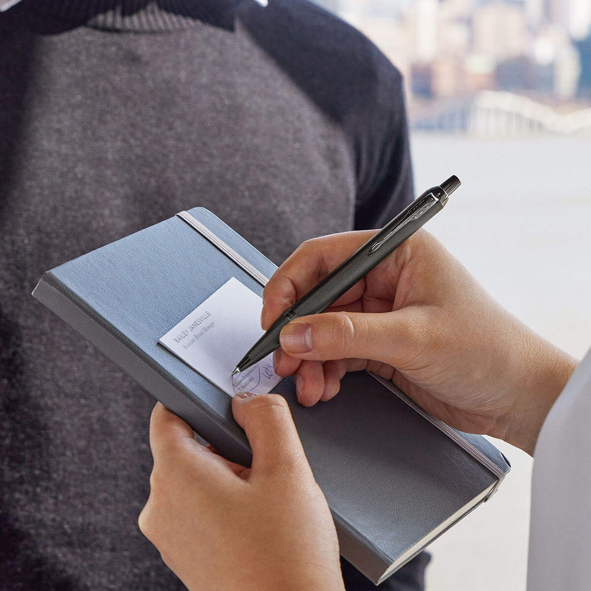 Zestaw prezentowy Parker IM Monochrome Bronze długopis w dłoni podczas pisania w notesie