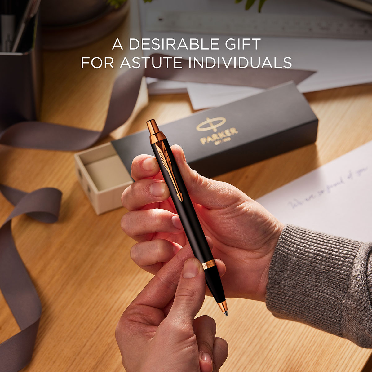 Długopis Parker IM Grey GT – ujęcie w dłoniach z pudełkiem prezentowym Parker i kartką na stole