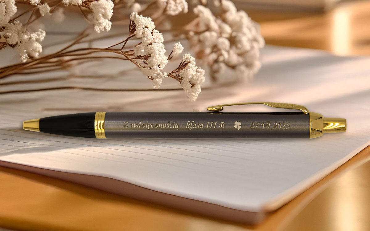 Elegancki długopis z grawerem „Z wdzięcznością – klasa III B 27 VI 2025” leżący na otwartym zeszycie obok suszonych kwiatów.