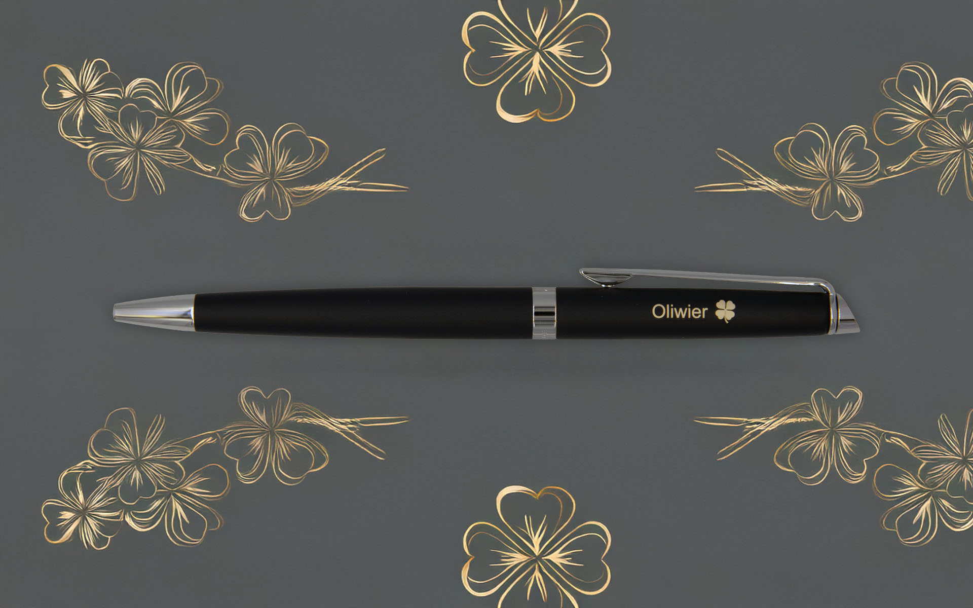 Elegancki czarny długopis z grawerem „Oliwier” i symbolem koniczyny na szarym tle z ozdobnymi złotymi motywami koniczyn