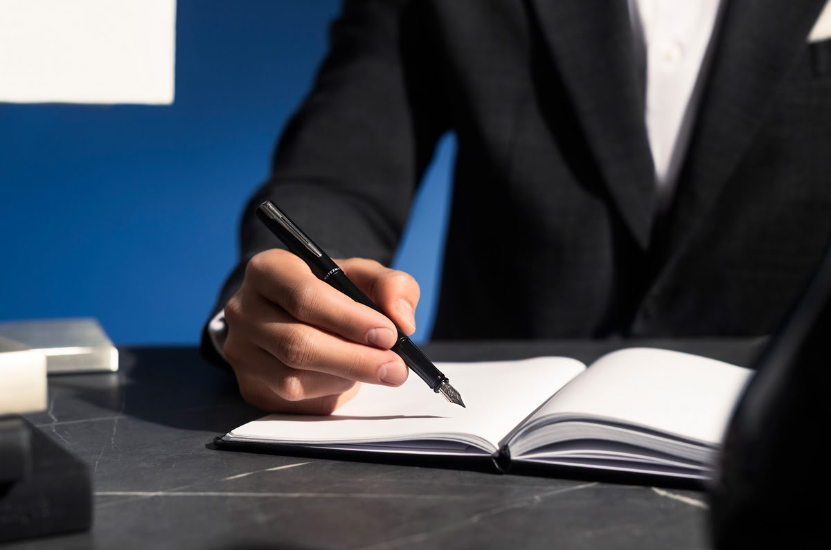 Pióro wieczne Waterman Allure czarne matowe CT w dłoni podczas pisania w notatniku na biurku.