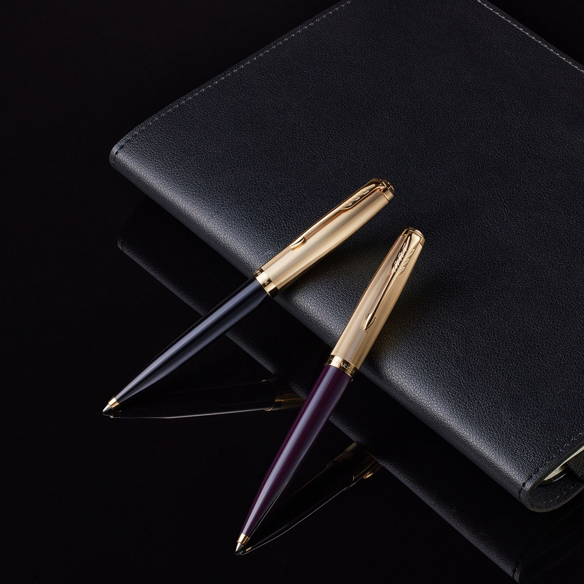 Długopis Parker 51 Deluxe Czarny GT z cyzelowaną złotą skuwką na czarnym organizerze obok wariantu Burgundy GT