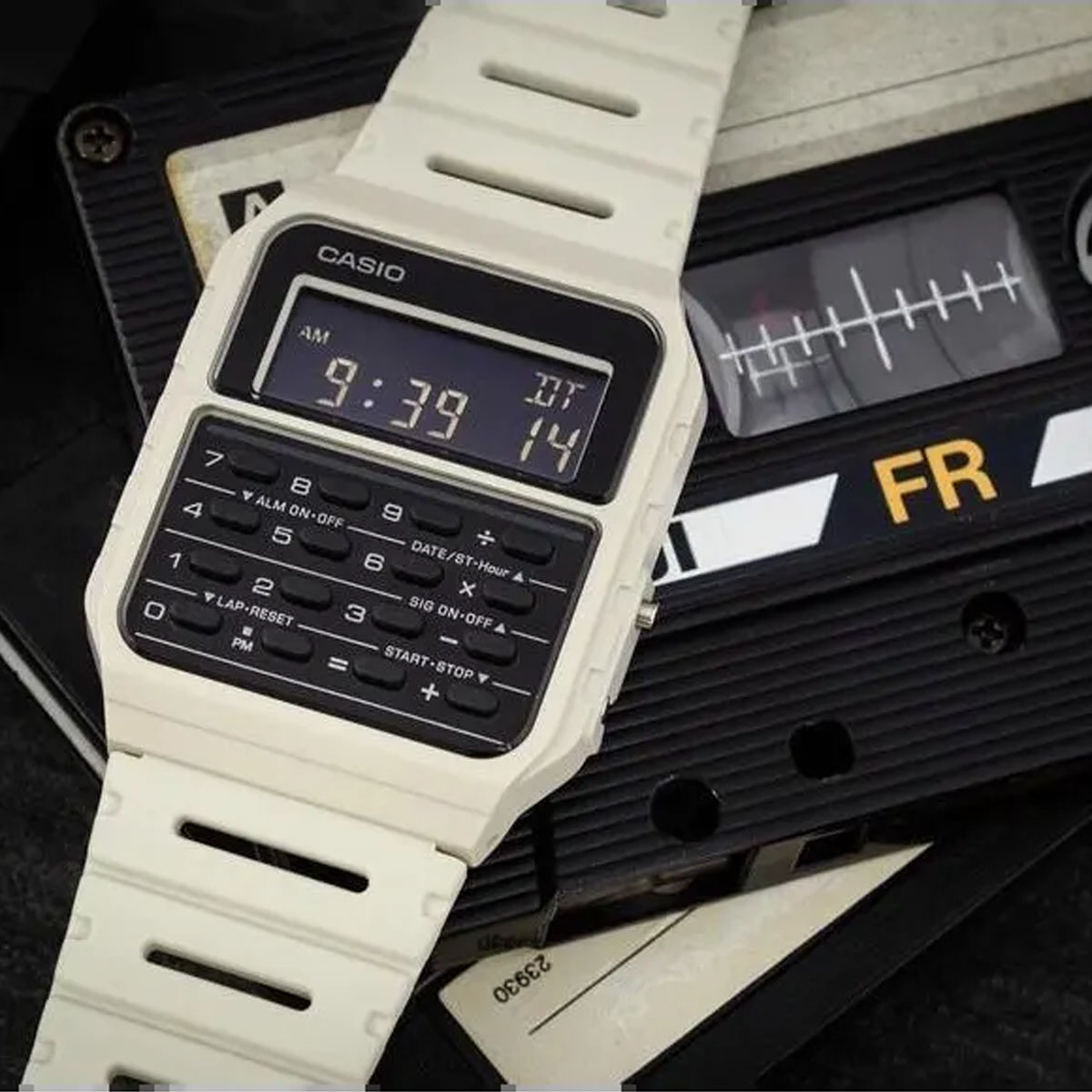 Biały zegarek Casio Calculator z kalkulatorem i cyfrowym wyświetlaczem na tle kasety magnetofonowej