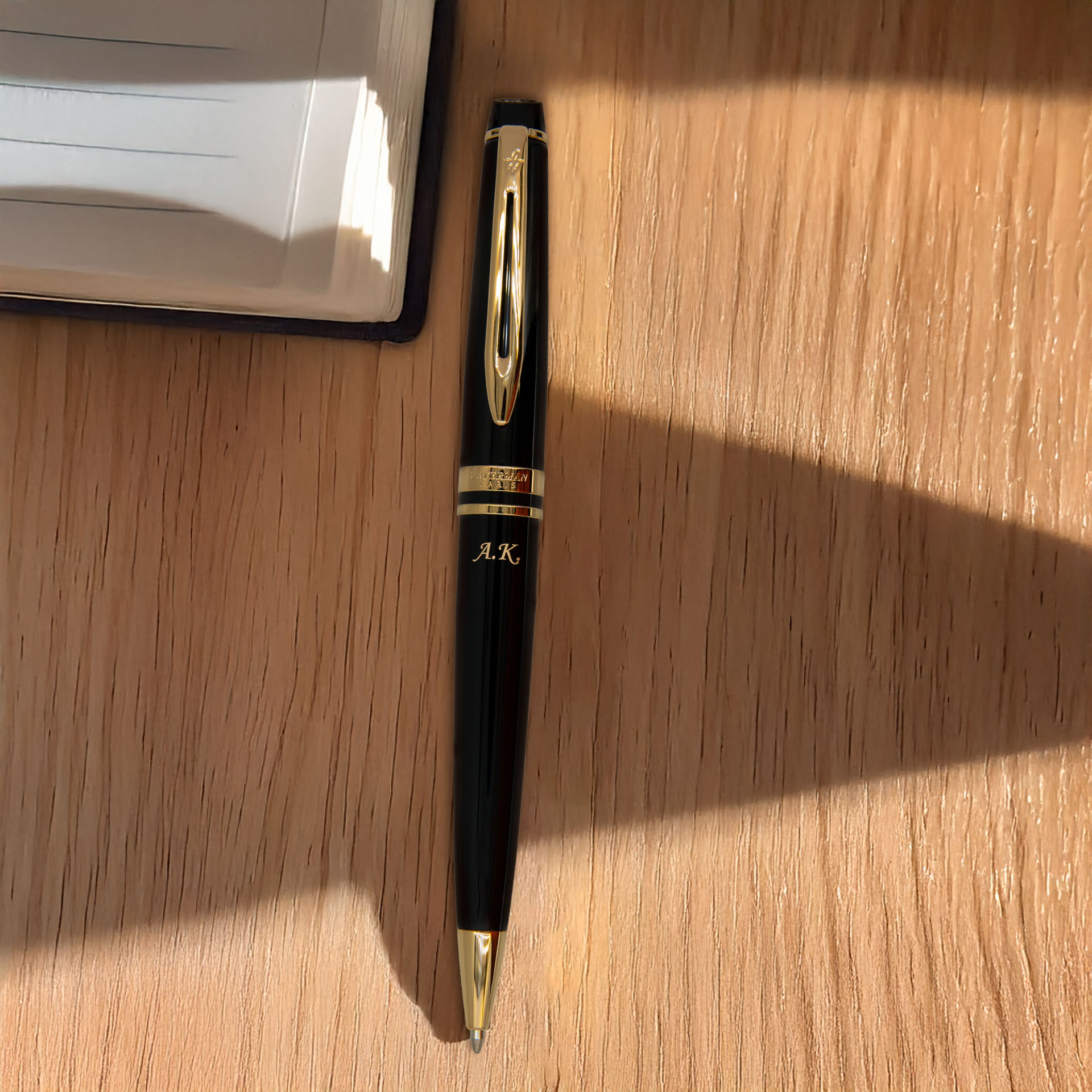 Długopis Waterman Expert z grawerem inicjałów, leżący na biurku koło notatnika