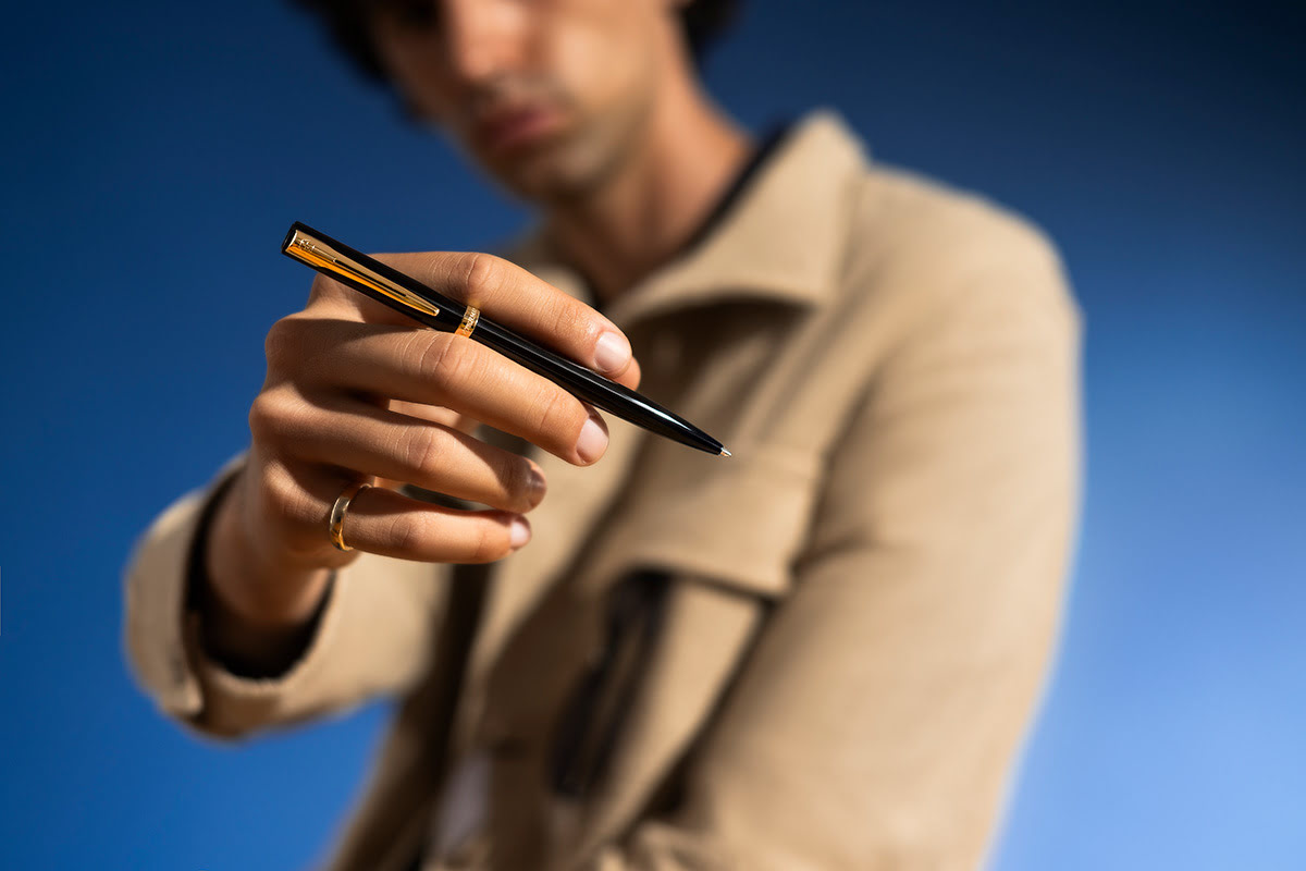 Długopis Waterman Allure Impression czarny GT trzymany w dłoni mężczyzny na niebieskim tle z eleganckim wykończeniem