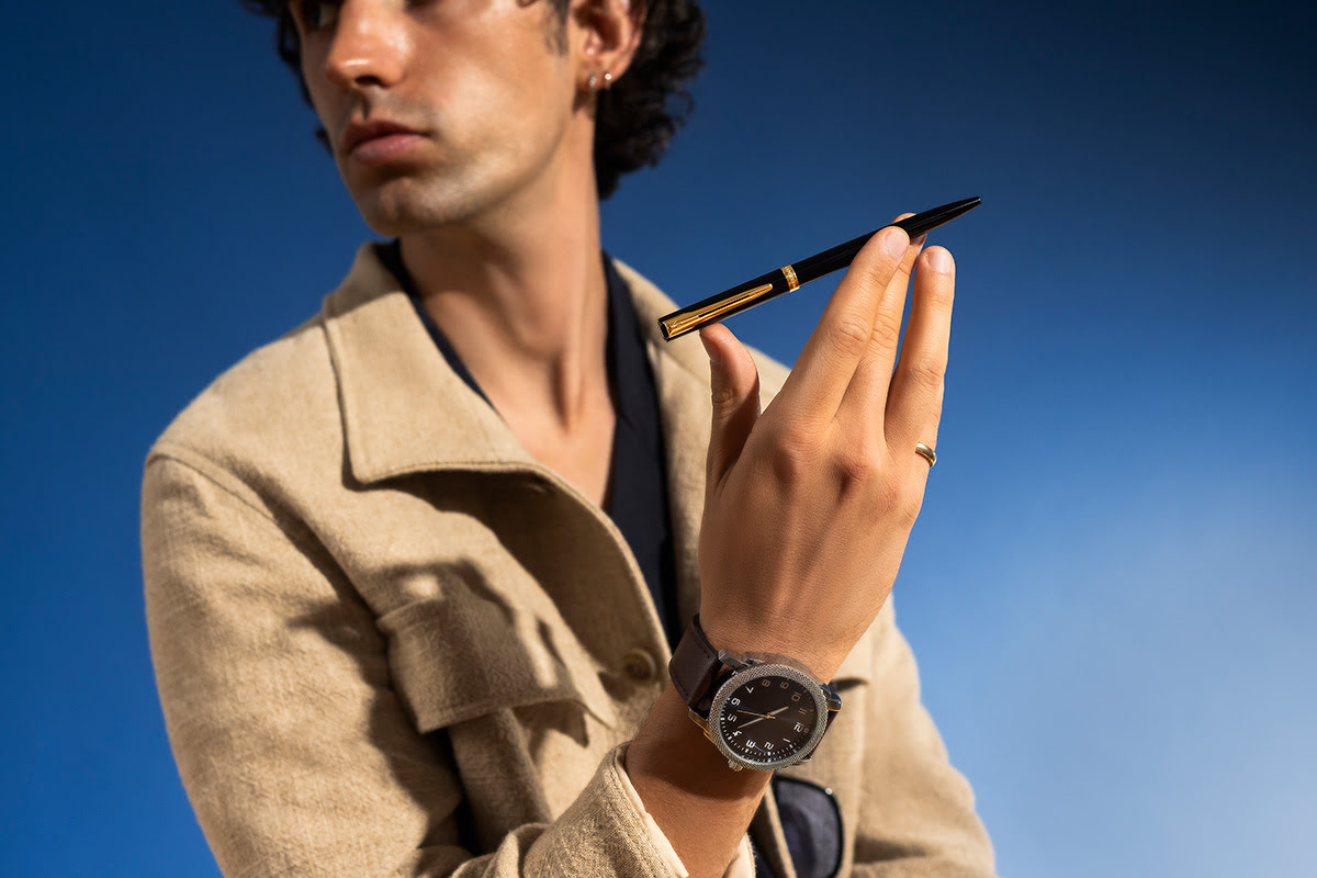 Długopis Waterman Allure Impression czarny GT trzymany w wyciągniętej dłoni na gładkim niebieskim tle