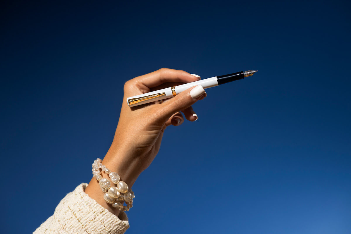 Pióro Waterman Allure Impression białe GT trzymane w dłoni kobiety na niebieskim tle z widoczną stalówką