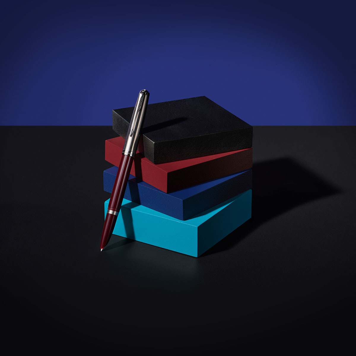 Parker 51_Shot05.jpg" alt="Pióro wieczne Parker 51 czerwone CT na tle kolorowych pudełek