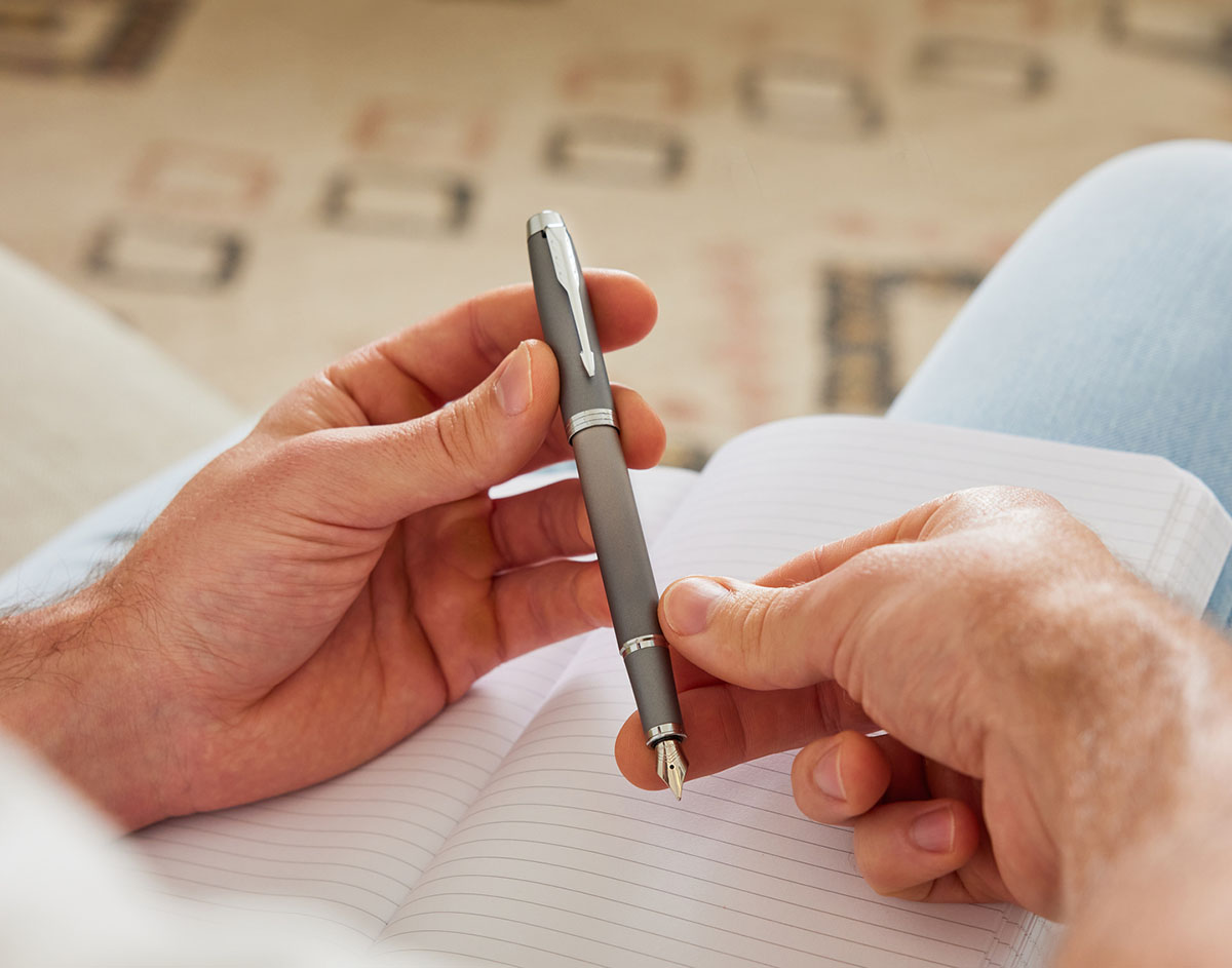 Mężczyzna trzymający stalowoszare pióro wieczne Parker Sonnet Grey GT nad otwartym notesem – widoczne detale klipsa i stalówki w chromowanym wykończeniu.
