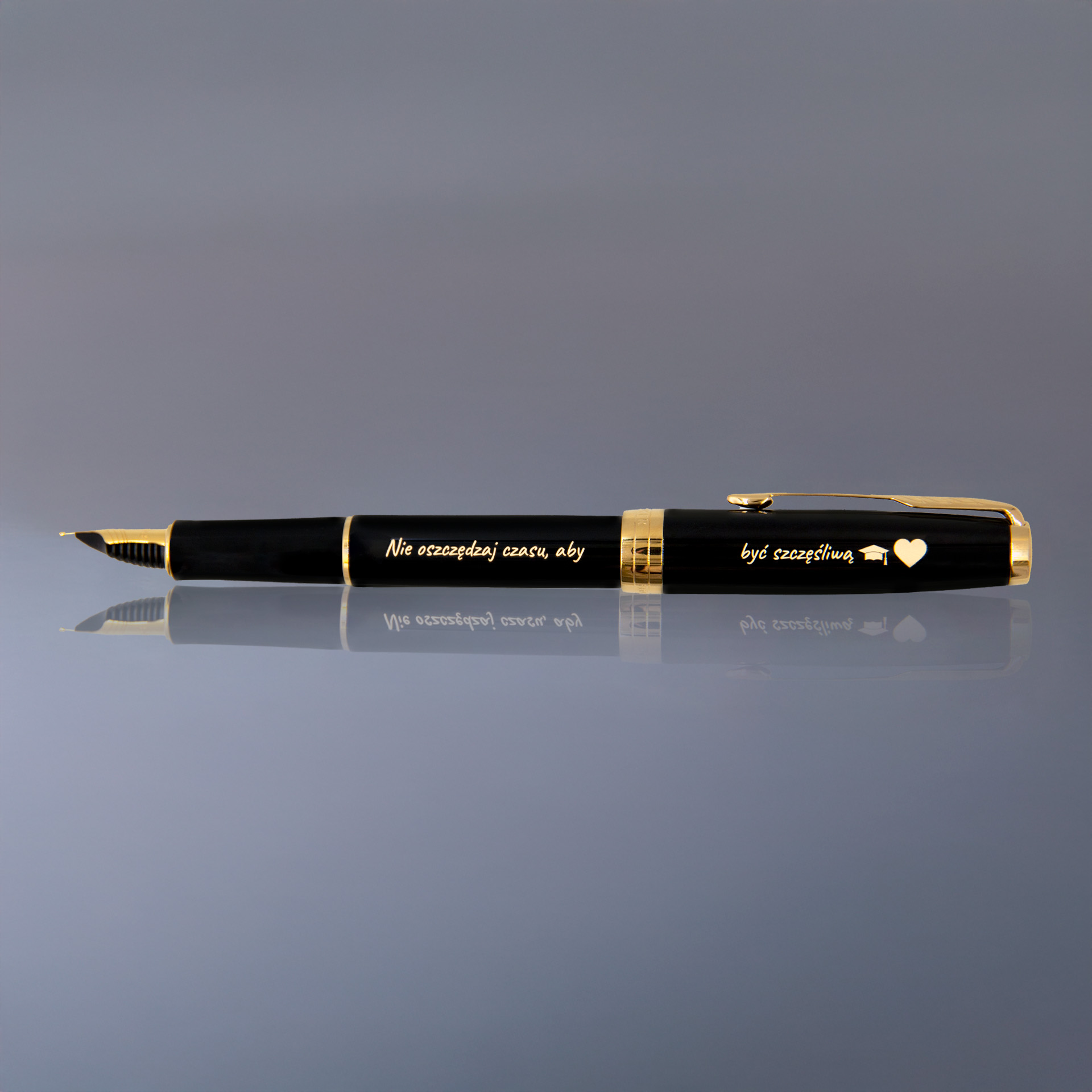 Pióro wieczne z grawerem „Nie oszczędzaj czasu, aby być szczęśliwą”, czarne z pozłacanymi wykończeniami, elegancko ułożone na lustrzanym tle.