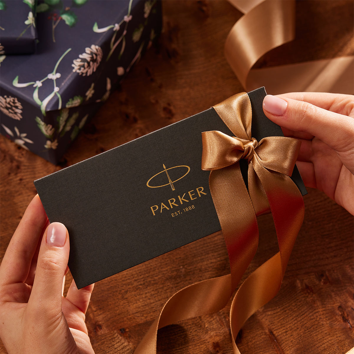Pudełko prezentowe Parker w kolorze czarnym z ozdobną złotą wstążką trzymane w dłoniach podczas Świąt