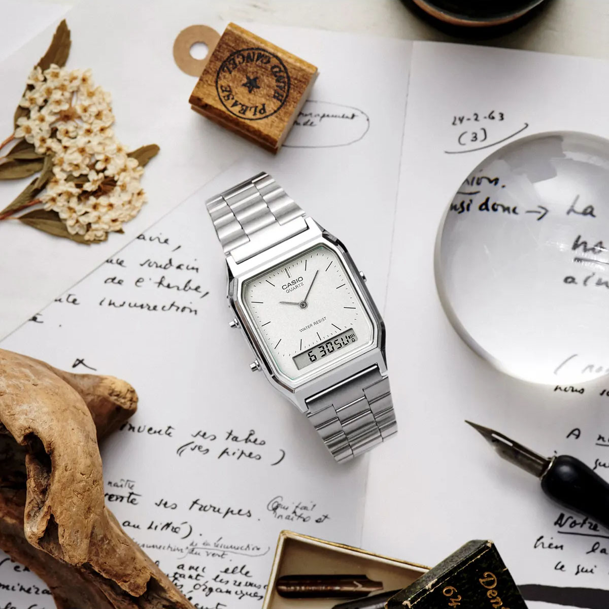 Srebrny zegarek Casio Vintage na stalowej bransolecie ułożony na notatkach obok pióra i lupy