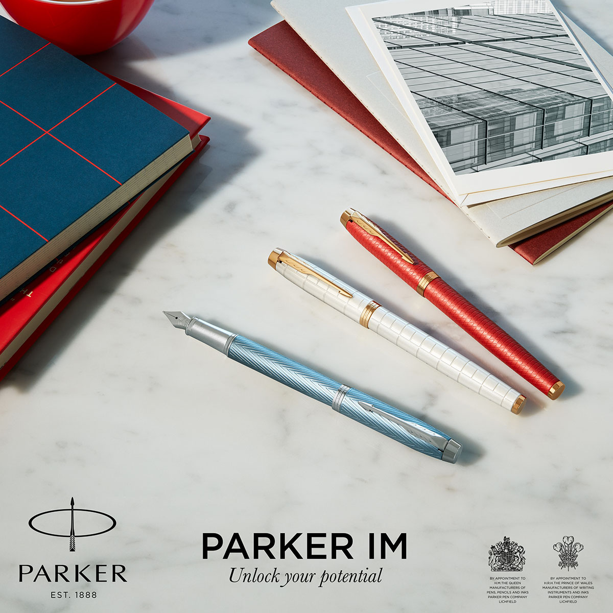 Kolekcja piór i długopisów Parker IM w eleganckich kolorach na biurku z dokumentami i notesami.