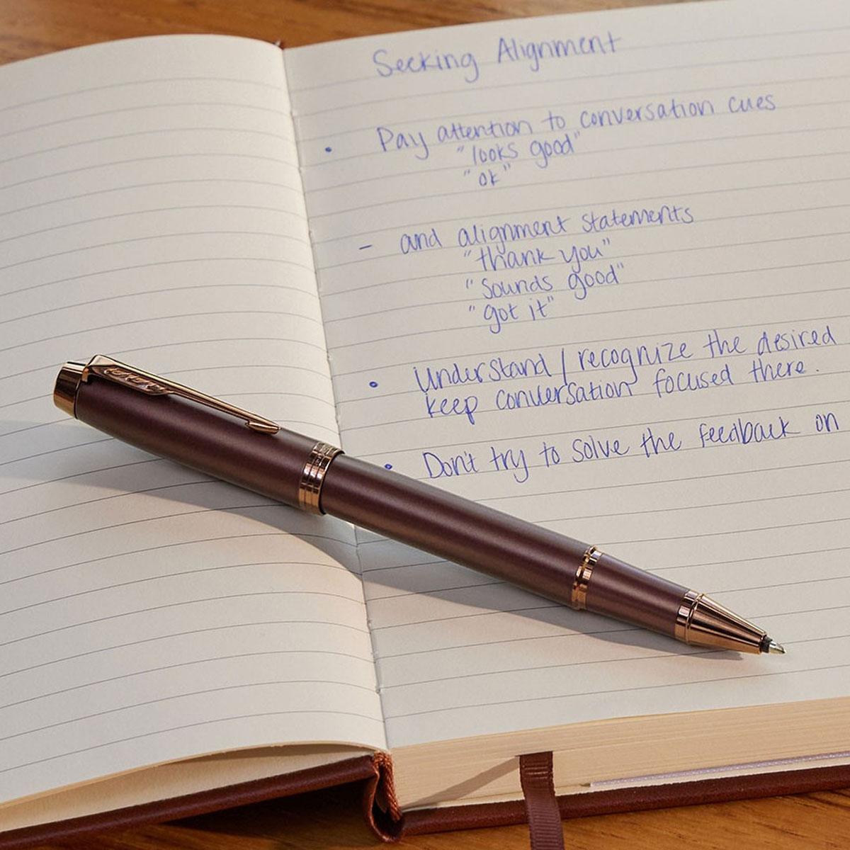 Elegancki długopis w kolorze bordowym leżący na otwartym notesie z odręcznymi notatkami.