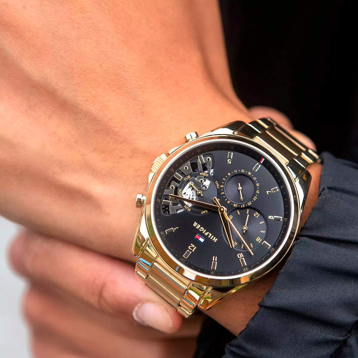 Zegarek męski Tommy Hilfiger 1710447 Baker złoty z czarną tarczą i bransoletą ze stali szlachetnej na nadgarstku.
