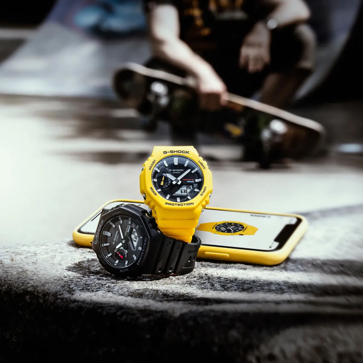 Zegarki Casio G-SHOCK w żółtej i czarnej wersji kolorystycznej obok smartfona