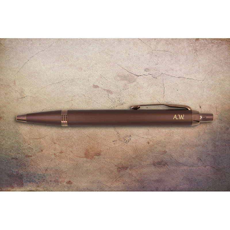 Burgundowy długopis Parker IM Monochrome z inicjałami „A.W.” na postarzałym tle w odcieniach beżu i brązu.