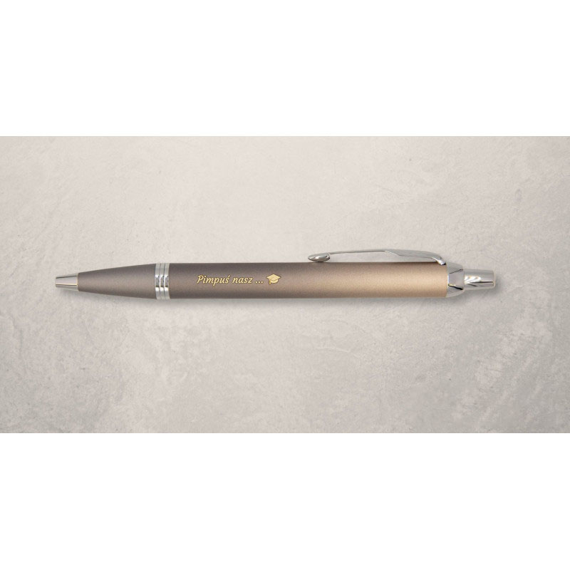 Długopis Parker IM w odcieniu szaro-złotym z grawerem „Pimpuś nasz…” i symbolem biretu, na jasnym tle.