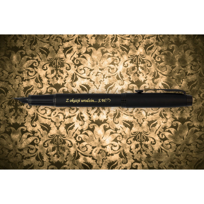 Czarne pióro wieczne Parker IM Achromatic z grawerem „Z okazji urodzin… S.W.” w złotym kolorze, umieszczone na tle w złoto-czarny ornament