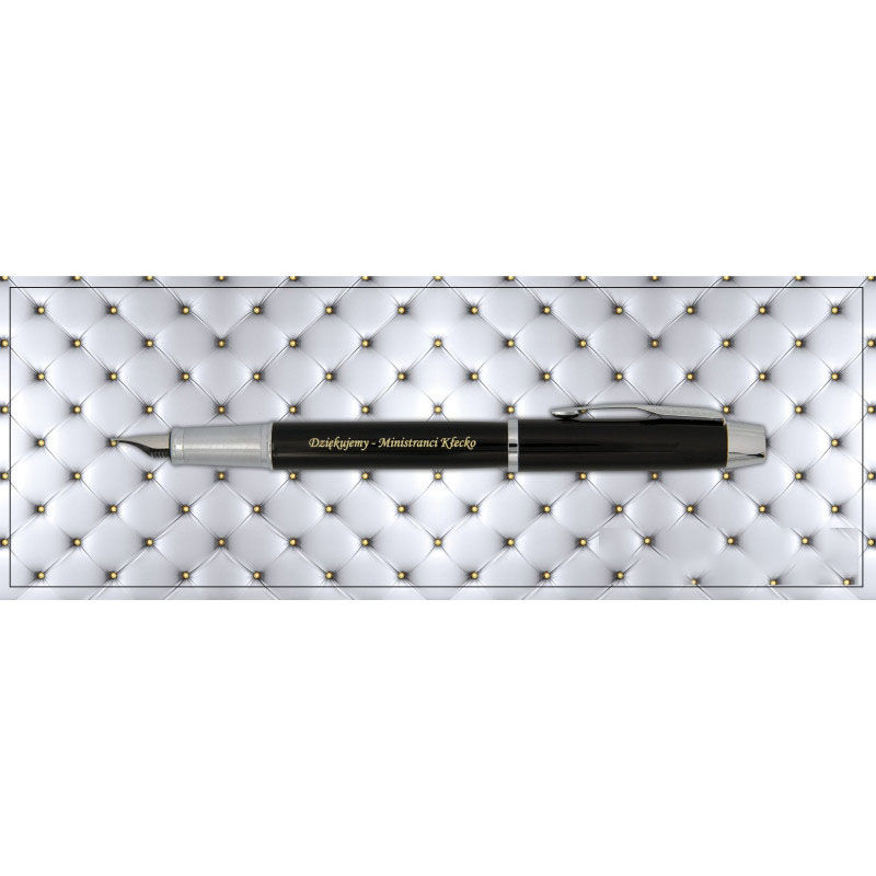 Czarne pióro wieczne Parker IM Black CT z chromowanymi wykończeniami i złotym grawerem „Dziękujemy – Ministranci Kłecko” na korpusie, sfotografowane na eleganckim tle imitującym pikowaną skórę z drobnymi, złotymi guzikami.