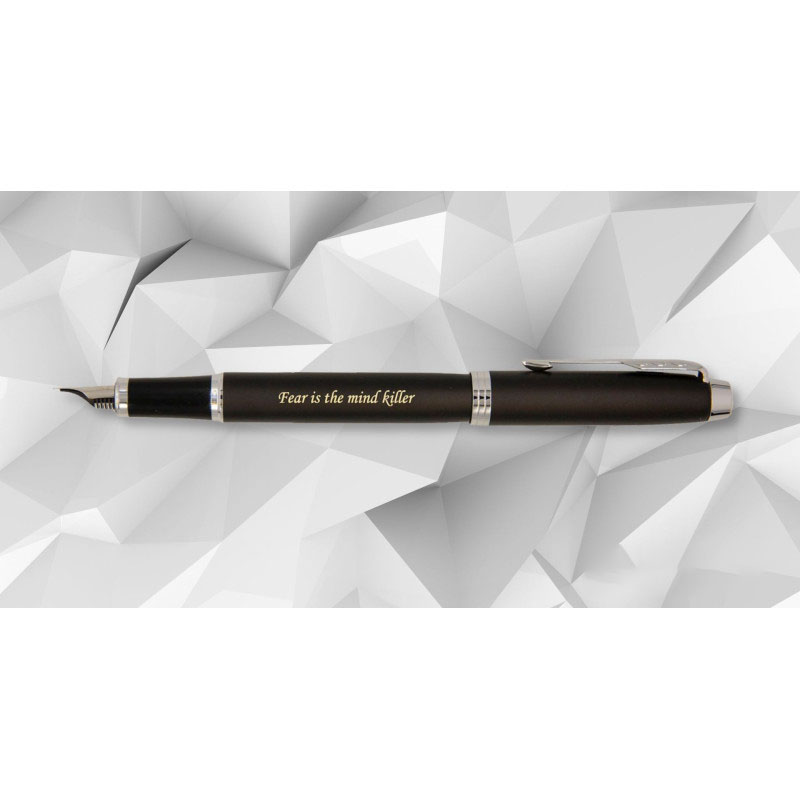 Czarne, matowe pióro wieczne Parker IM CT ze srebrnymi wykończeniami i klipsem w kształcie strzały, z wygrawerowanym złotym napisem „Fear is the mind killer”. Pióro zaprezentowane jest na geometrycznym tle w odcieniach bieli i szarości, przypominającym tr