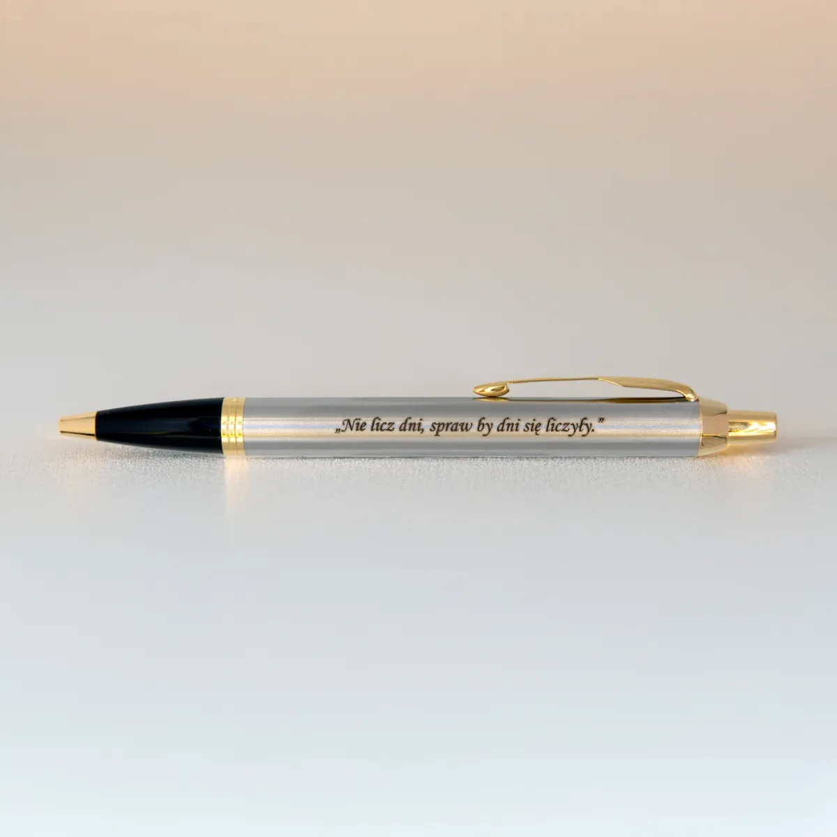 Długopis Parker IM Brushed Metal GT (1931670) z grawerem „Nie licz dni, spraw by dni się liczyły.” sfotografowany na jasnym tle w ciepłym, miękkim świetle.