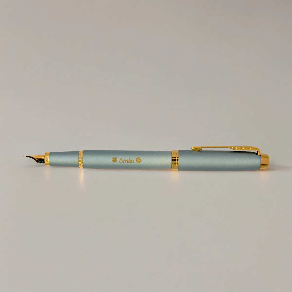 Pióro wieczne Parker IM Rituals Turquoise Green (2203892) z grawerem „Lenka” i motywem łapek, sfotografowane na jasnym tle w miękkim, ciepłym świetle.