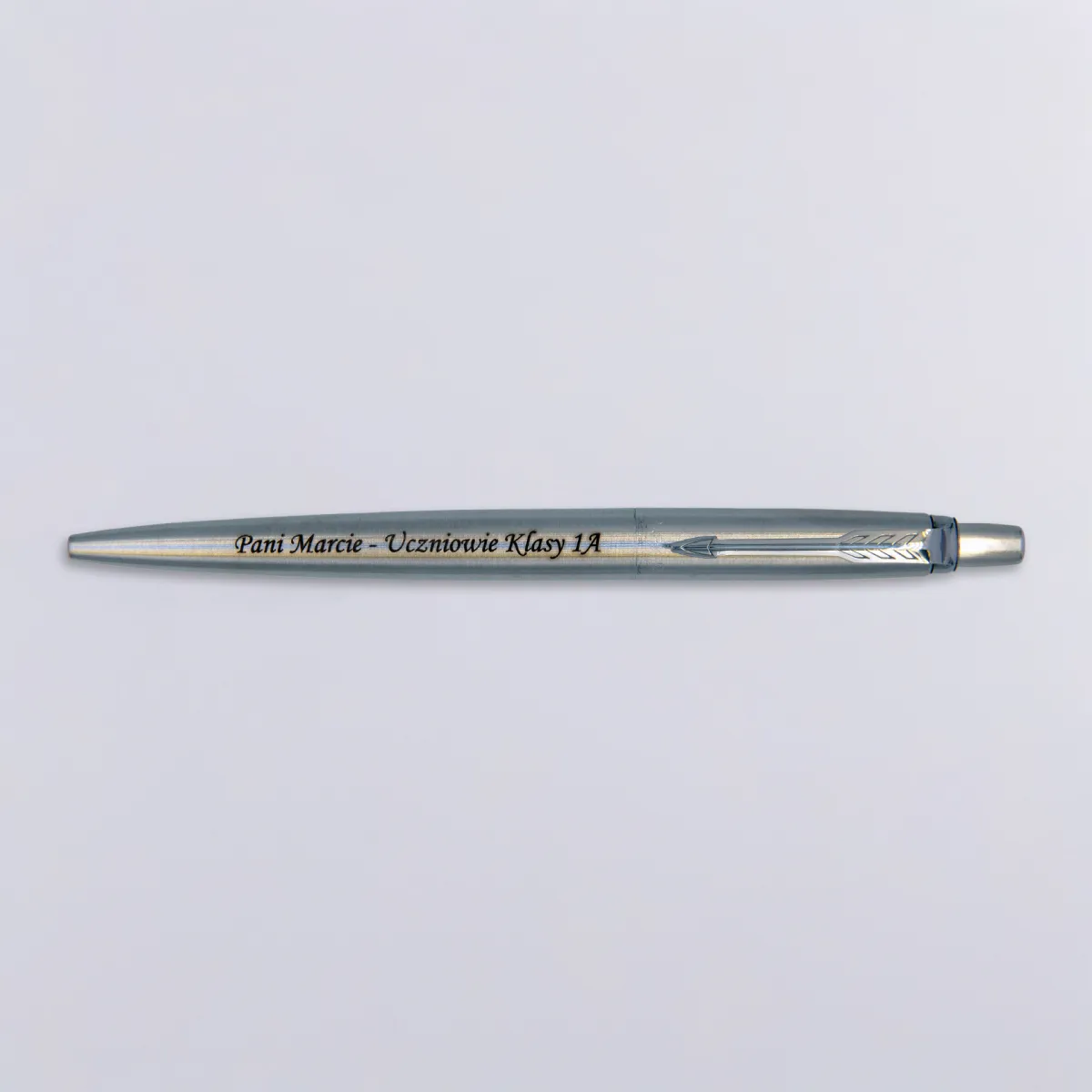 Długopis Parker Jotter Stalowy Matowy CT (1953170) z grawerem &bdquo;Pani Marcie &ndash; Uczniowie Klasy 1A&rdquo;, ułożony na jasnym tle, w minimalistycznym ujęciu podkreślającym elegancję i symboliczny charakter prezentu.