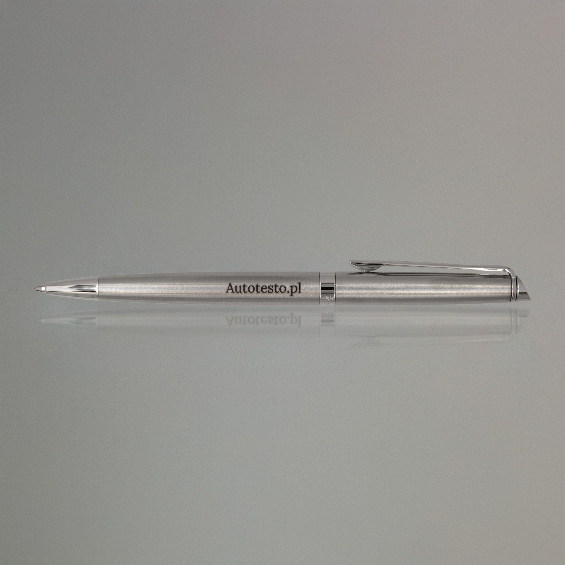 Długopis Waterman Hemisphere stalowy CT (S0920470) z grawerem Autotesto.pl, eleganckie ujęcie na lustrzanej powierzchni z delikatnym odbiciem i neutralnym tłem.