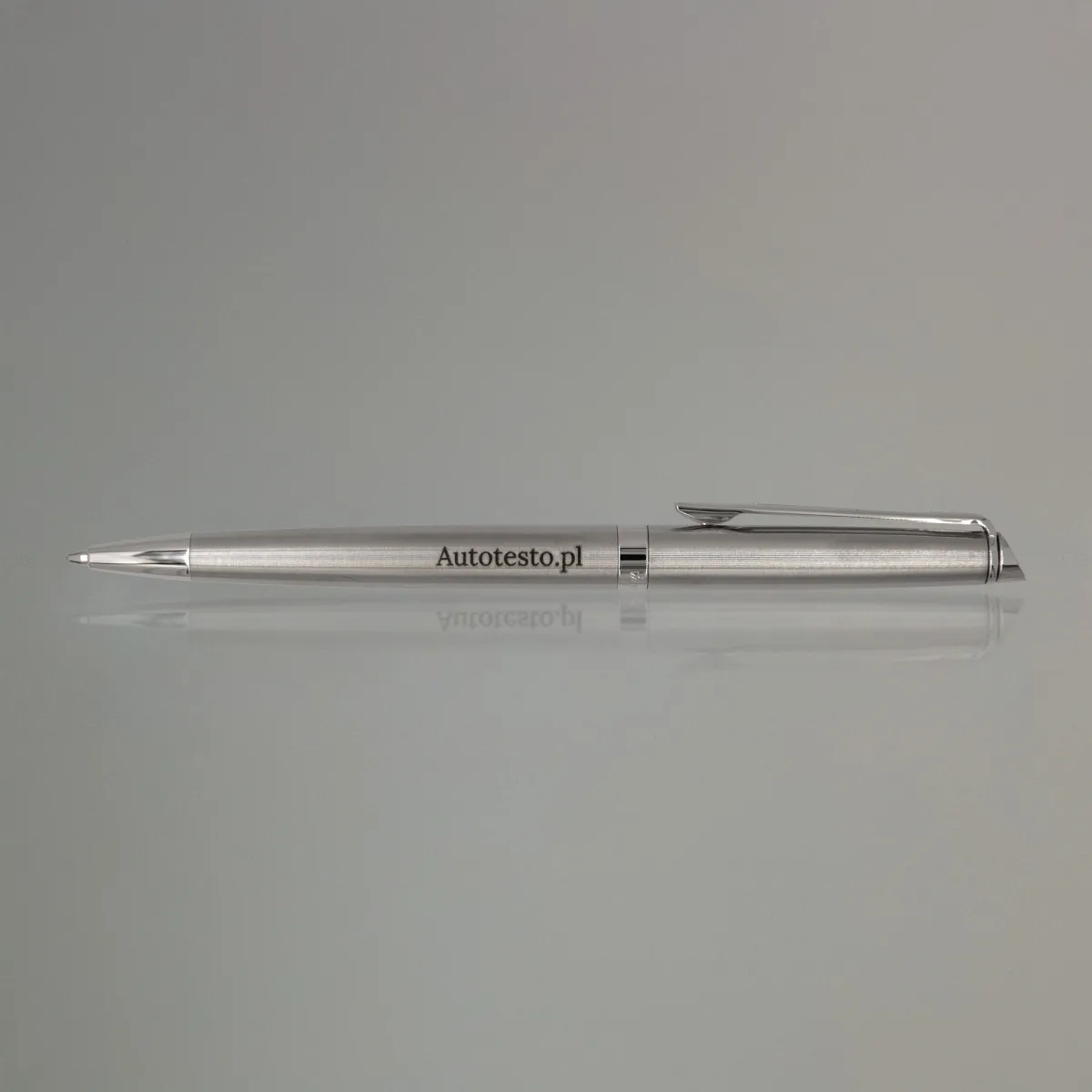 Długopis Waterman Hemisphere stalowy CT (S0920470) z grawerem Autotesto.pl, eleganckie ujęcie na lustrzanej powierzchni z delikatnym odbiciem i neutralnym tłem.