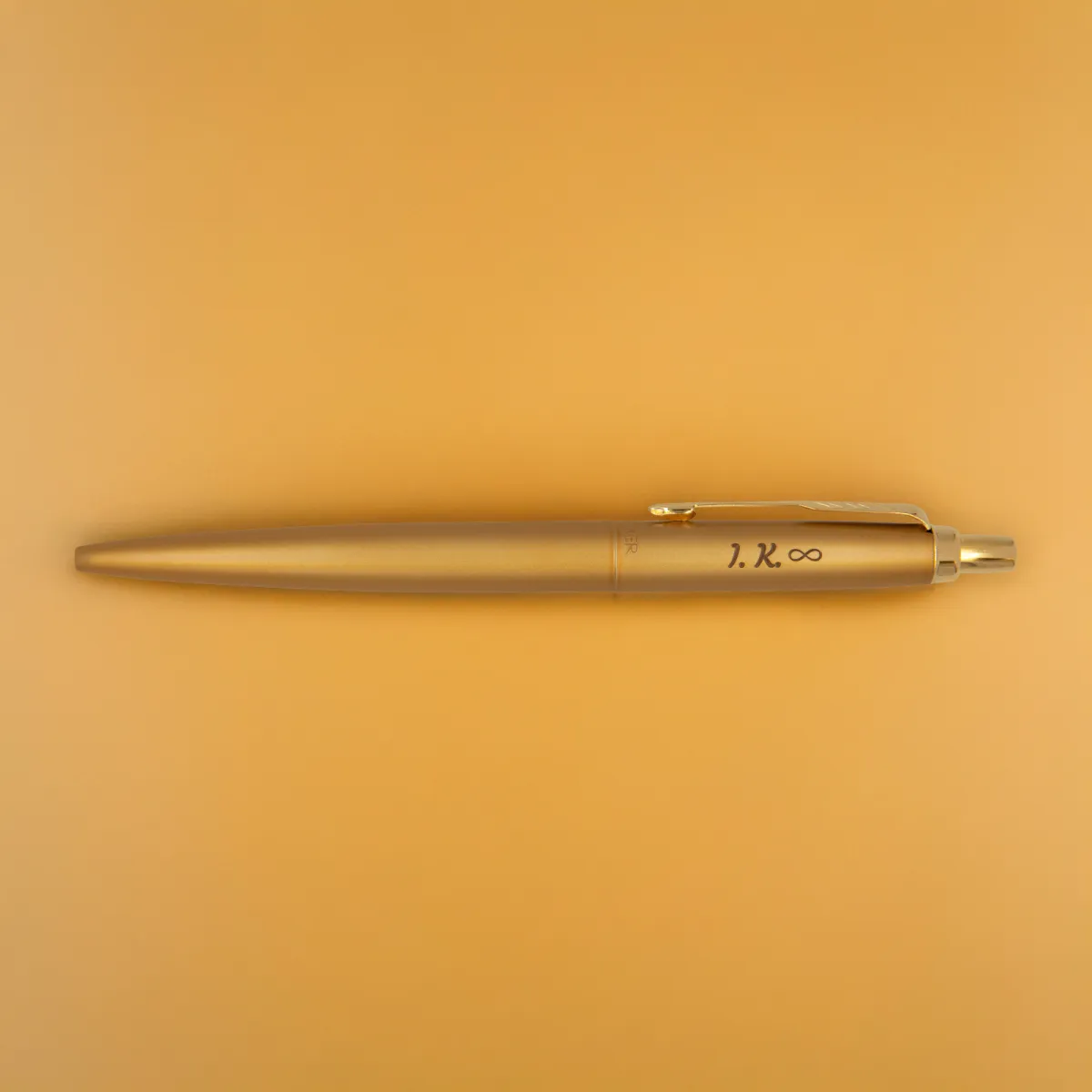 Długopis Parker Jotter XL Monochrome Gold z grawerem &bdquo;I.K. &infin;&rdquo;, sfotografowany na złotym tle w ciepłym świetle, podkreślającym jego jednolity kolor i połysk.