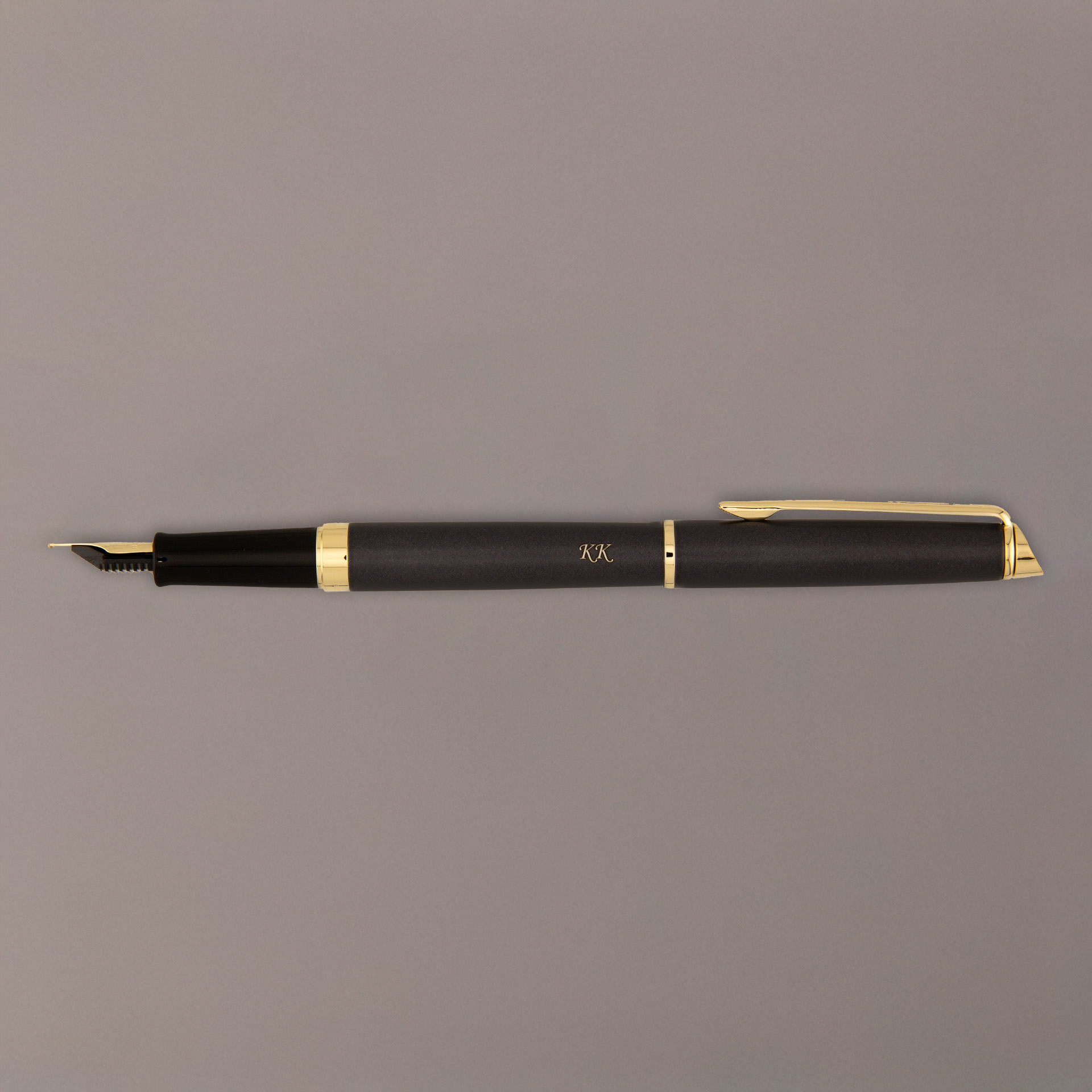 Czarne pióro wieczne z pozłacanymi detalami i grawerem „K.K.” na szarym tle.