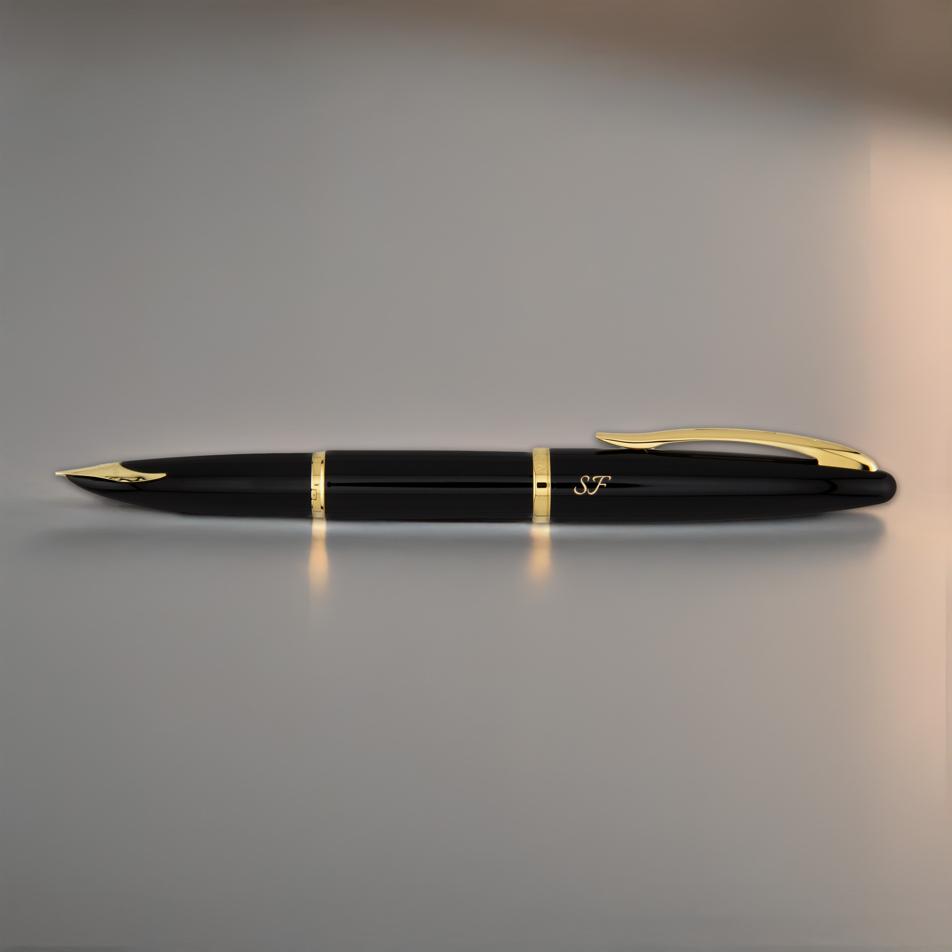 Czarny Waterman Carène Black Sea GT z inicjałami „SF” leży na gładkim, jasnym tle, ukazując złote detale.