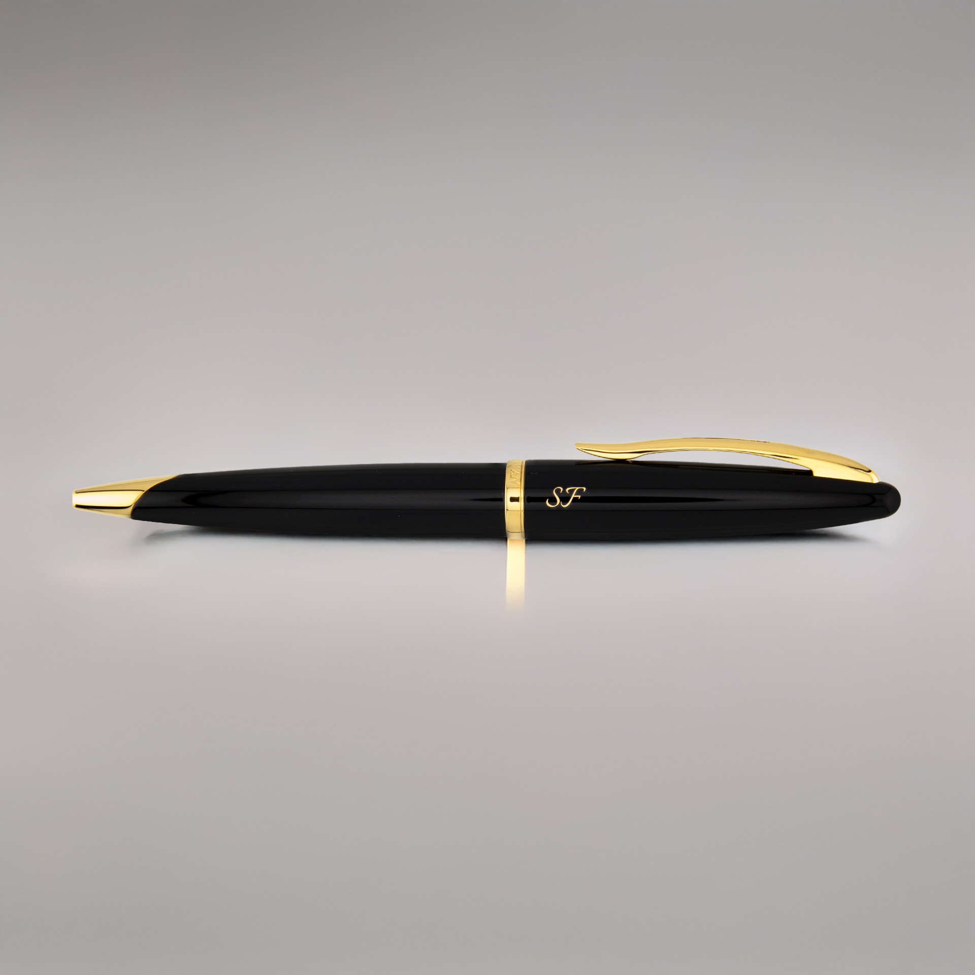 Czarny długopis Waterman Carène GT z inicjałami „SF” leży na gładkim, jasnym tle, ukazując złote detale.