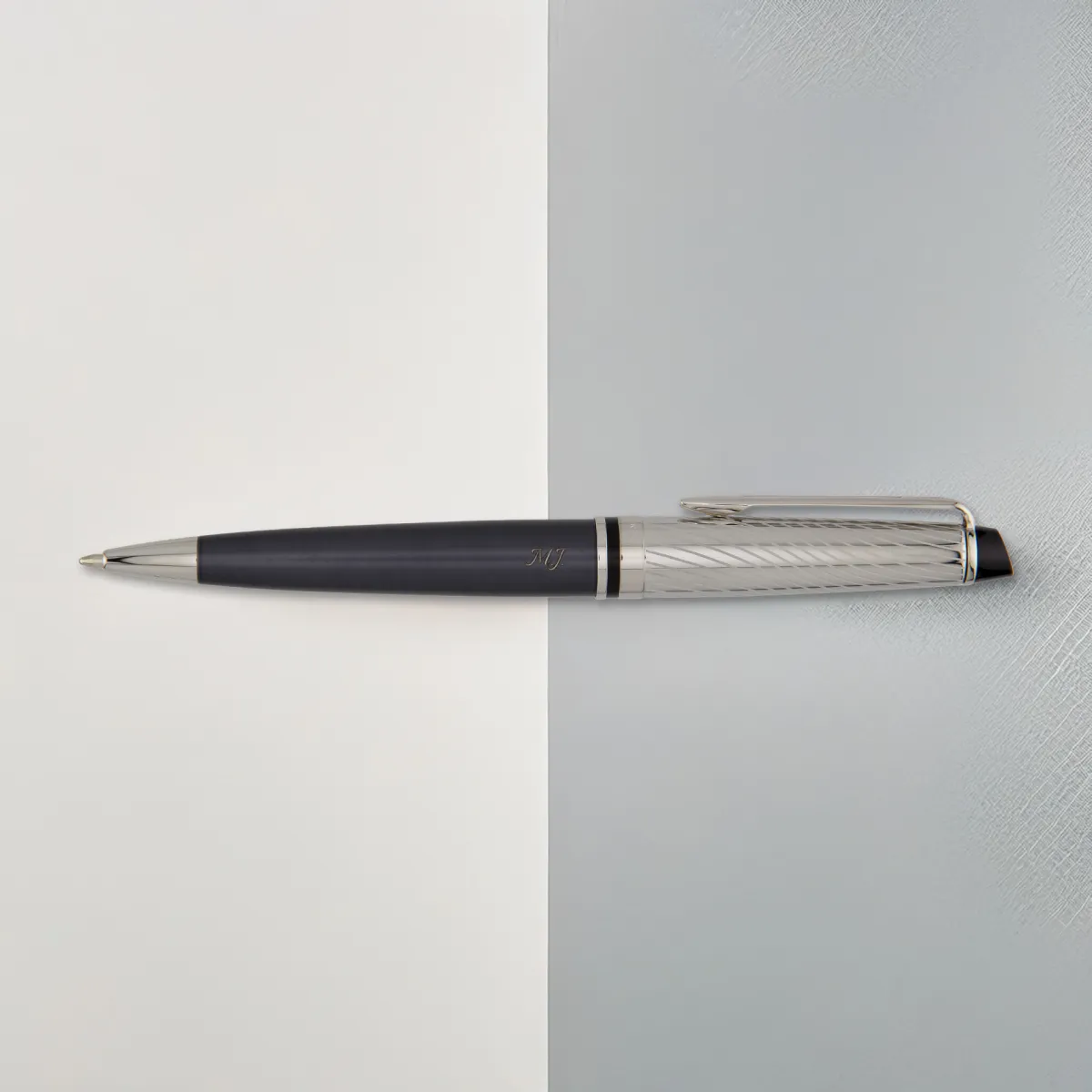 Długopis Waterman Expert Deluxe w grafitowym wykończeniu leży na dwukolorowym tle, ukazując metaliczną fakturę skuwki.