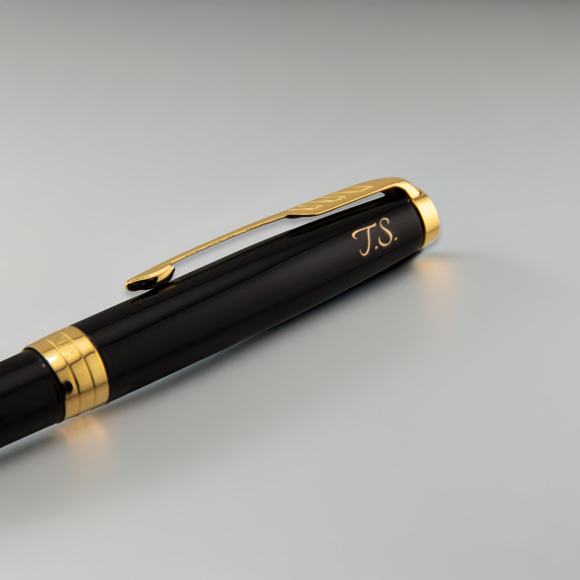Czarne pióro z eleganckimi złotymi detalami i grawerem „J.S.”, ujęcie z bliska na jasnym, neutralnym tle.
