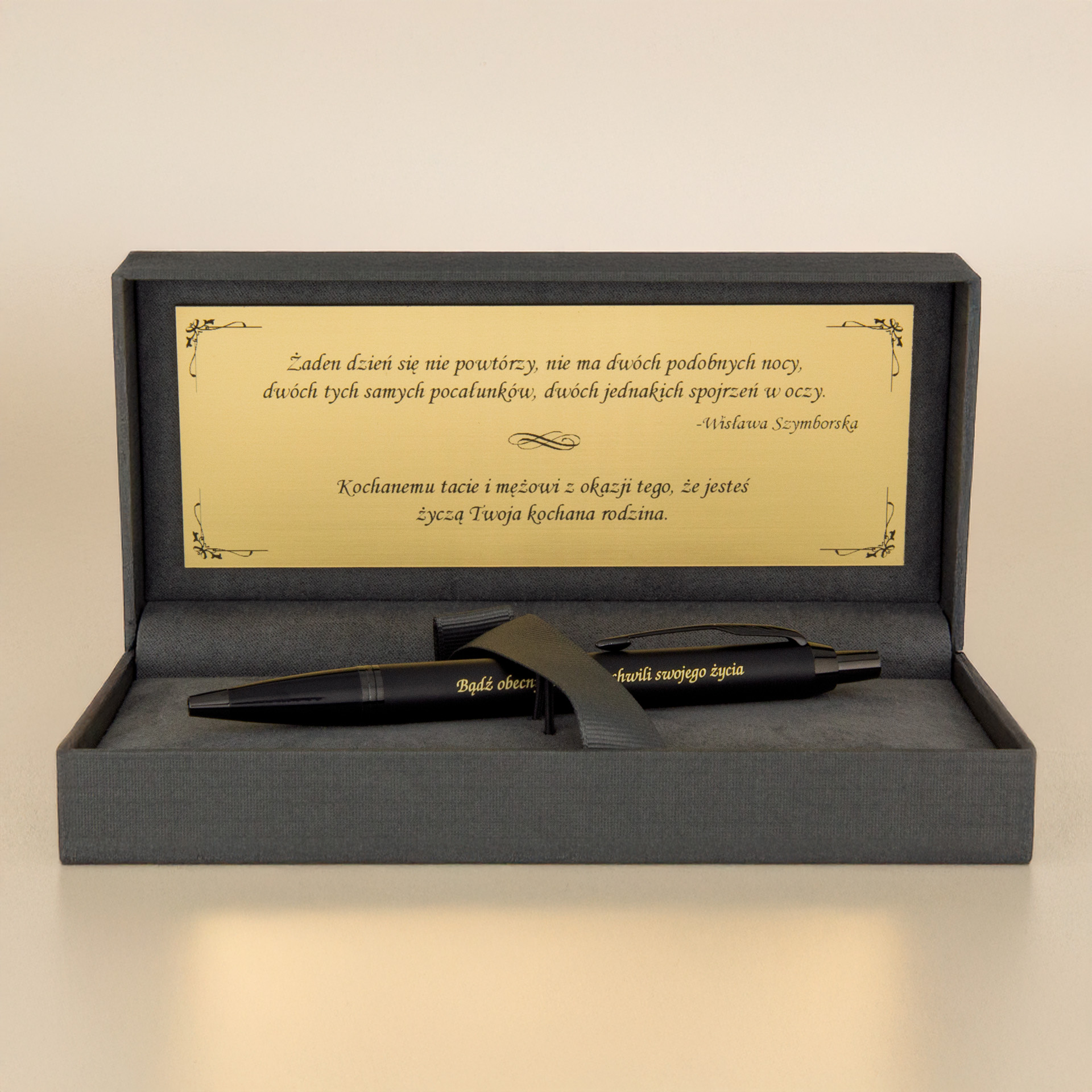 Eleganckie etui prezentowe z czarnym długopisem i złotą tabliczką z cytatem Wisławy Szymborskiej oraz dedykacją, na jasnym tle.