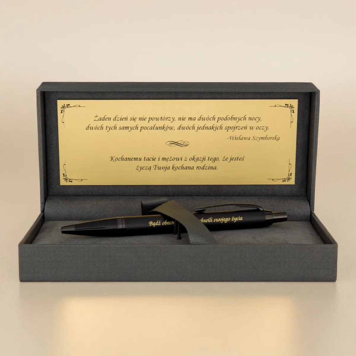Eleganckie etui prezentowe z czarnym długopisem i złotą tabliczką z cytatem Wisławy Szymborskiej oraz dedykacją, na jasnym tle.