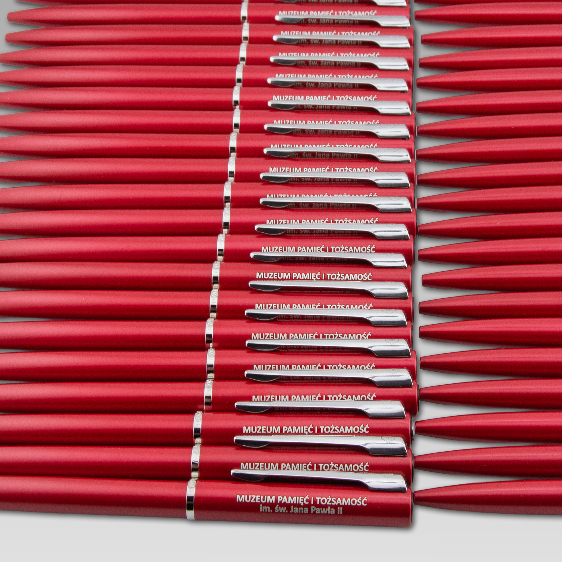 Czerwone długopisy z logo Muzeum Pamięć i Tożsamość ułożone w rzędzie.