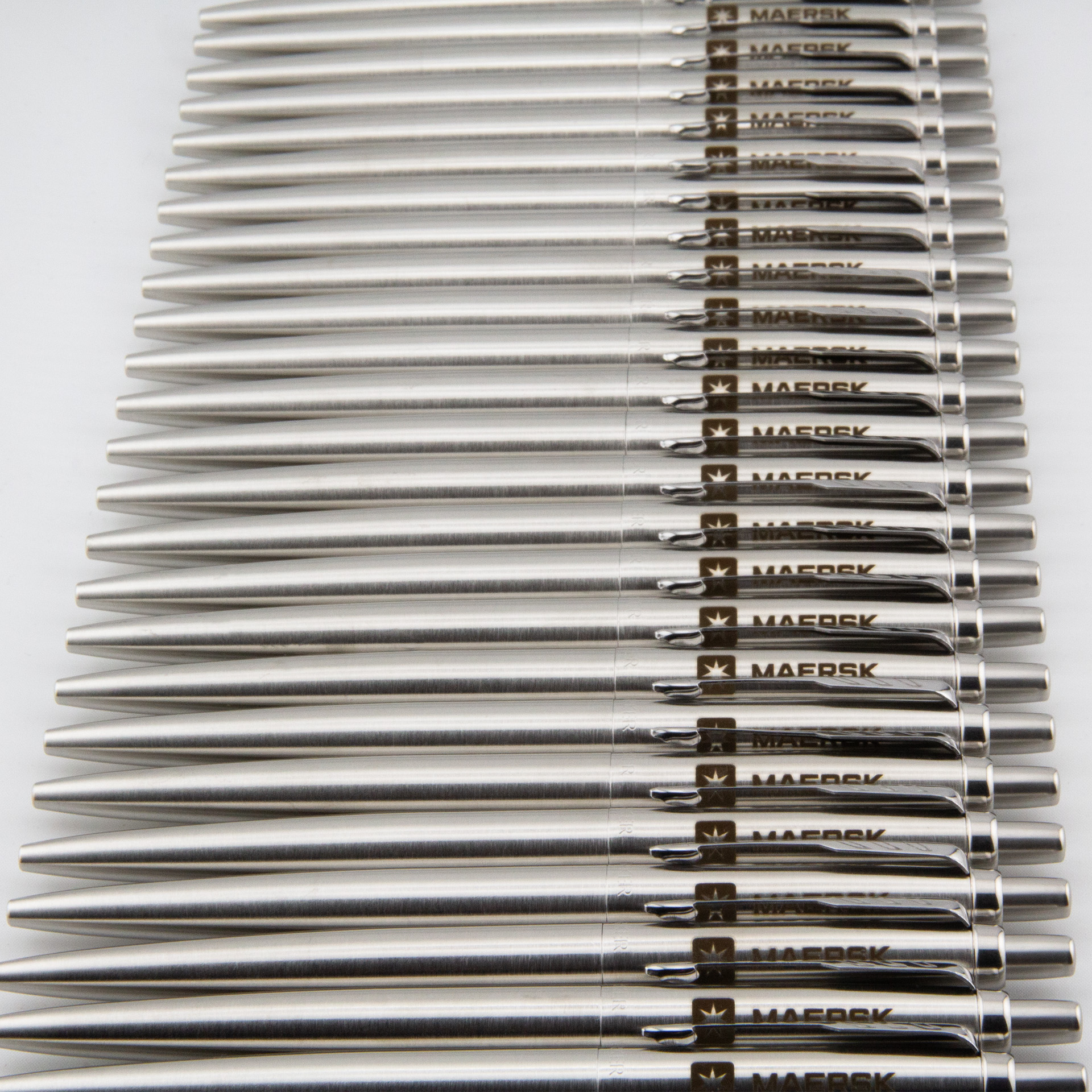 Metalowe długopisy z logo Maersk ułożone w rzędzie.