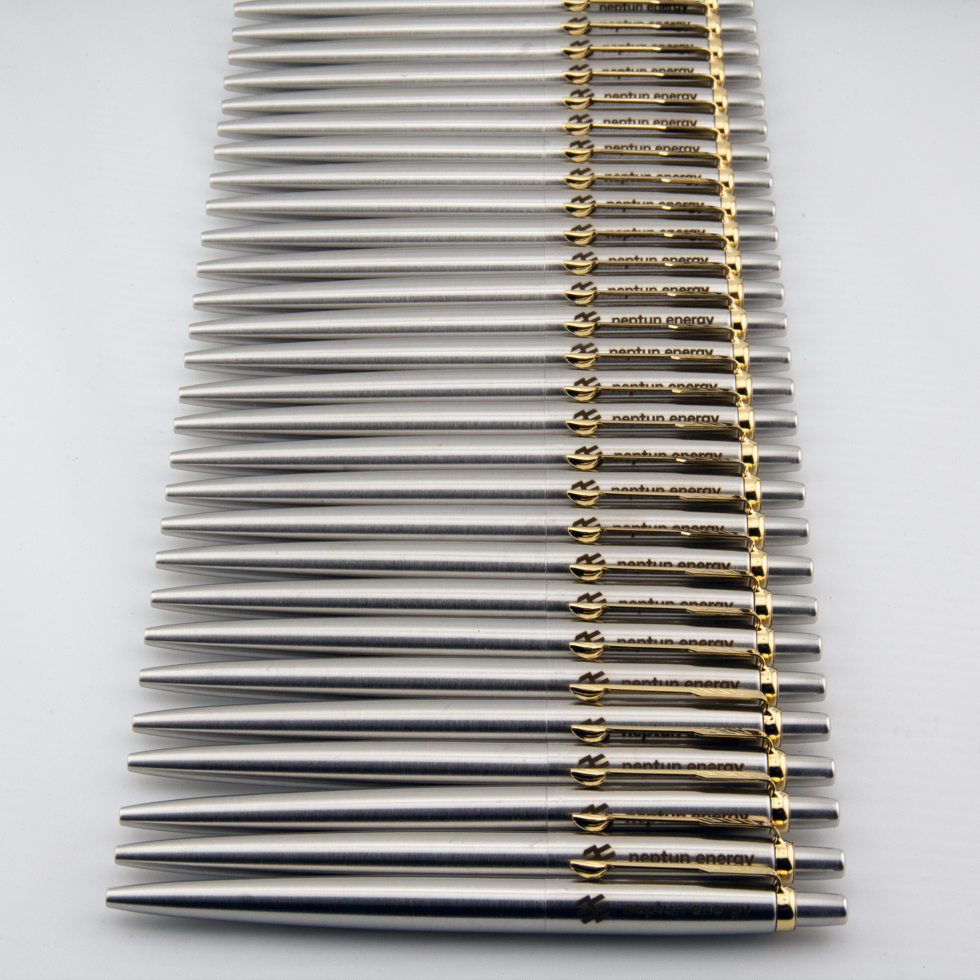Srebrne metalowe długopisy z logo Neptun Energy i złotymi klipsami ułożone w rzędzie
