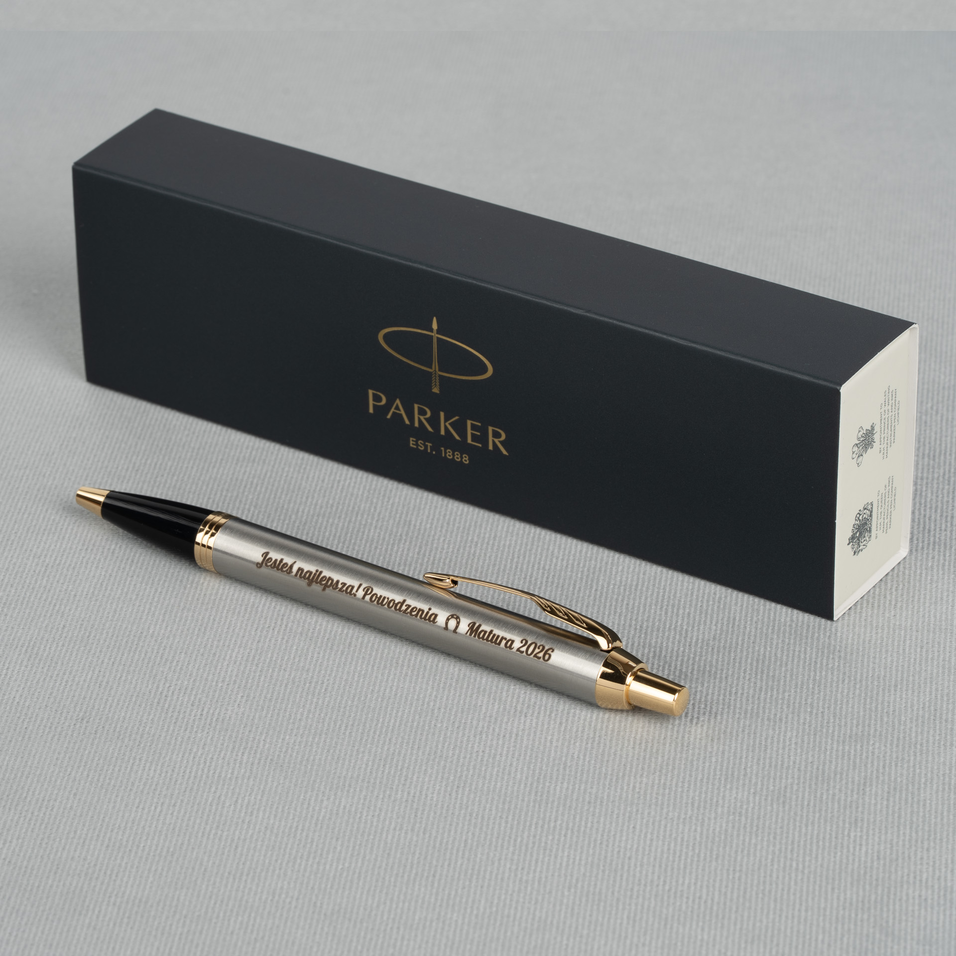 Długopis Parker IM Brushed Metal GT z grawerem „Jesteś najlepsza! Powodzenia Matura 2026” na jasnym tle z pudełkiem Parker w tle
