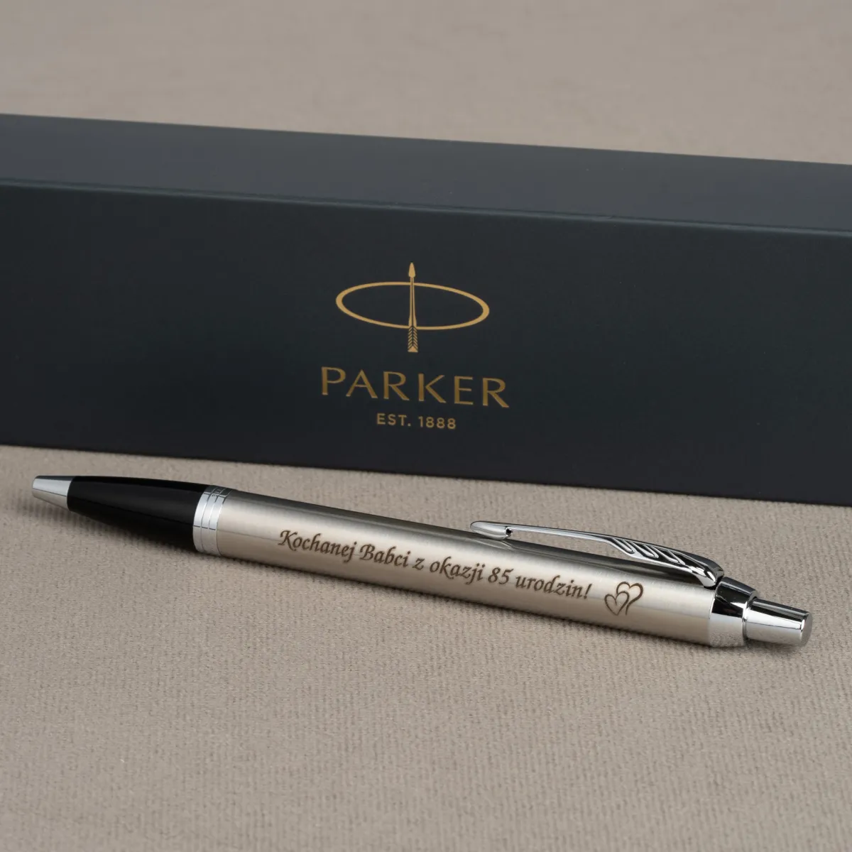 Długopis Parker IM Stainless Steel CT z grawerem &bdquo;Kochanej Babci z okazji 85 urodzin!&rdquo; na tle eleganckiego pudełka Parker.