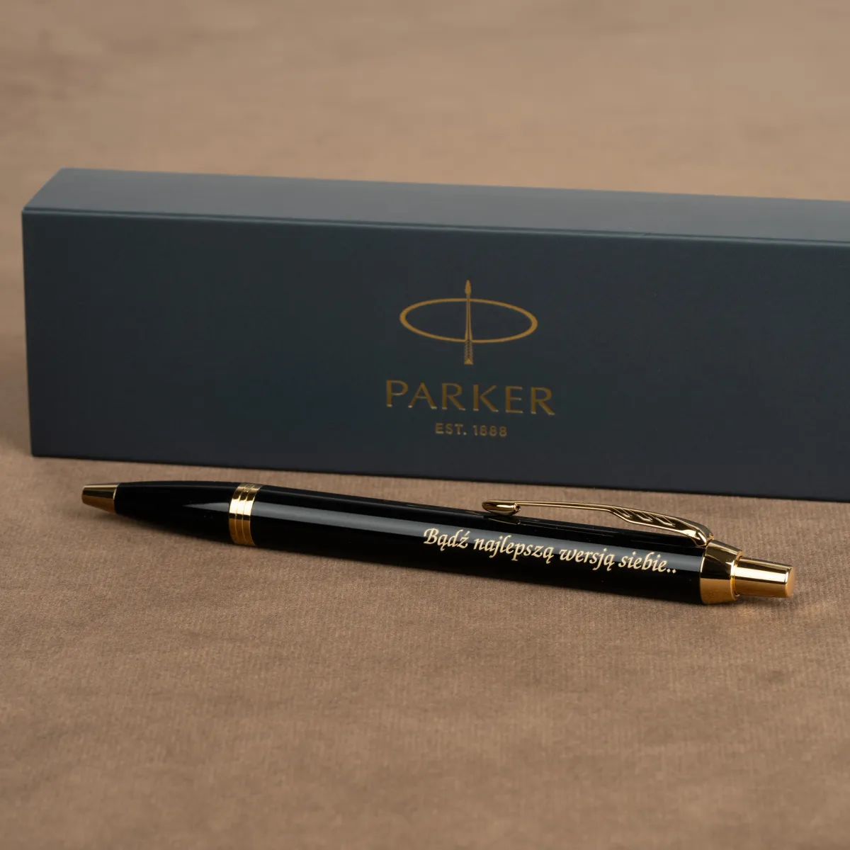 Długopis Parker IM Czarny GT z motywującym grawerem „Bądź najlepszą wersją siebie...” ustawiony na tle eleganckiego pudełka Parker.