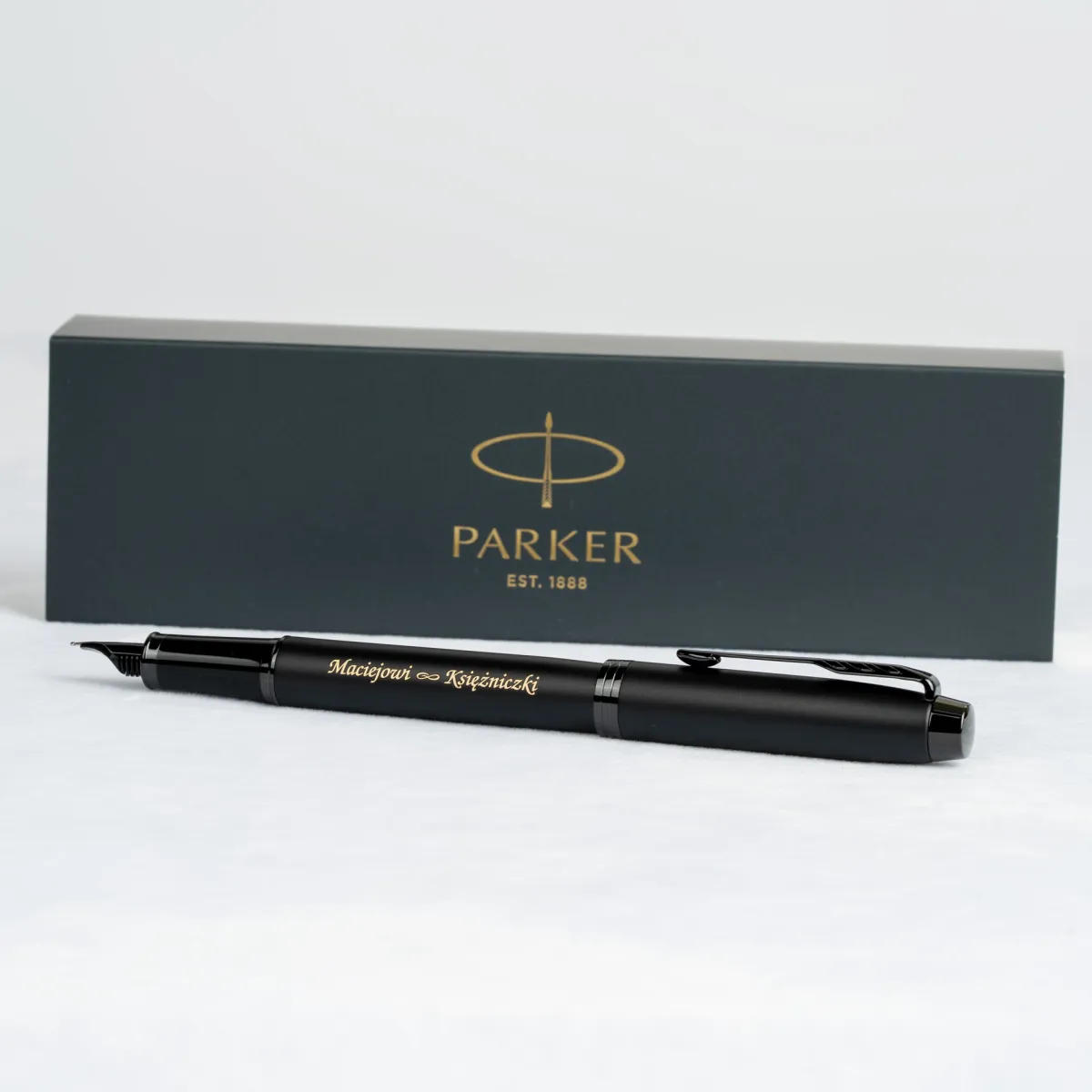 Pióro wieczne Parker IM Achromatic Czarne z personalizowanym grawerem „Maciejowi ∞ Księżniczki” na tle pudełka Parker.