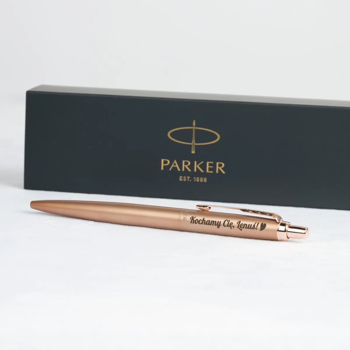 Długopis Parker Jotter XL Monochrome Pink Gold z grawerem „Kochamy Cię, Lenus!” na tle firmowego pudełka Parker.