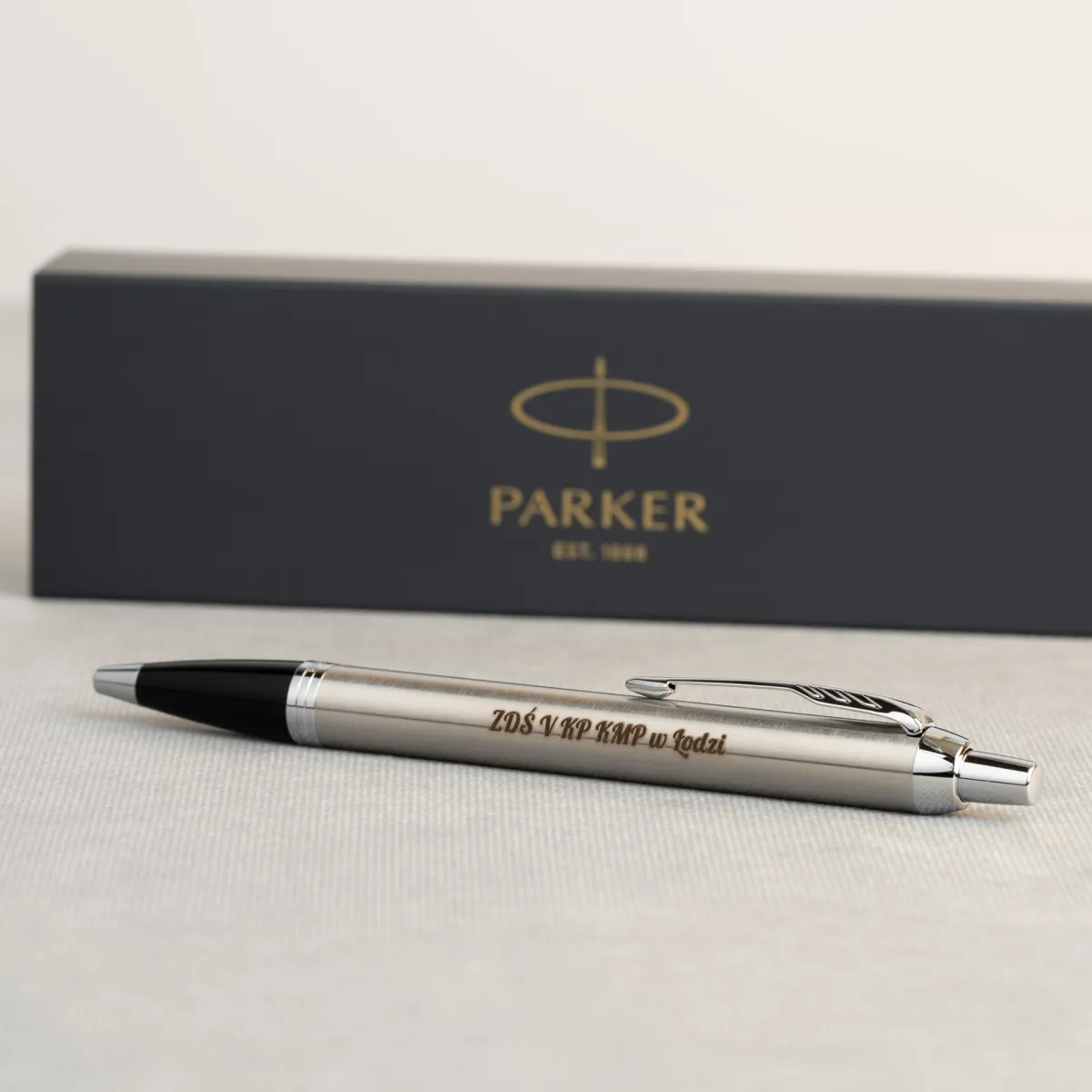 Długopis Parker IM Stainless Steel CT z grawerem &bdquo;ZDS V KP KMP w Łodzi&rdquo; na tle eleganckiego pudełka Parker.